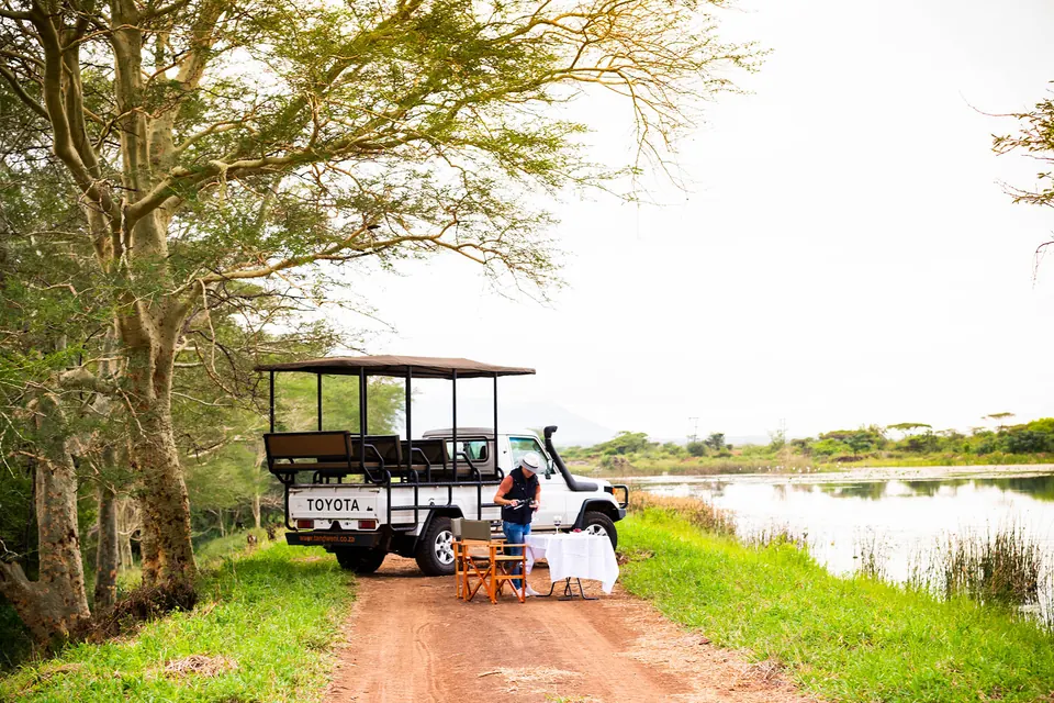 An open game-drive vehicle parked beside a lake for a bush picnic